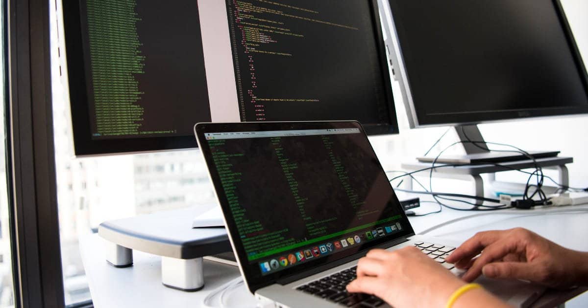A developer working at a laptop with code on an external monitor