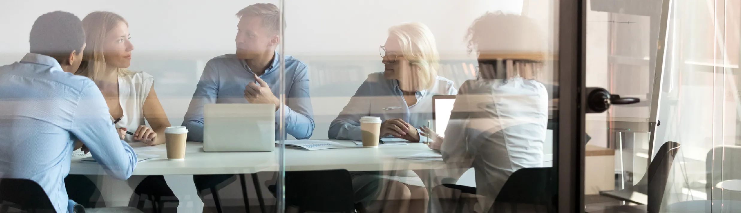 A team meeting around a conference table, seen through a glass wall